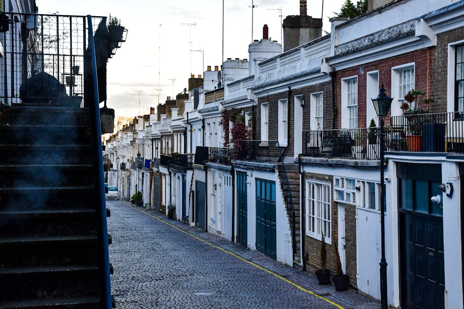 A black-and-white aerial photograph of a residential street showing closely spaced houses and terraced properties. The street is lined with parked cars on each side, including sedans and hatchbacks, w