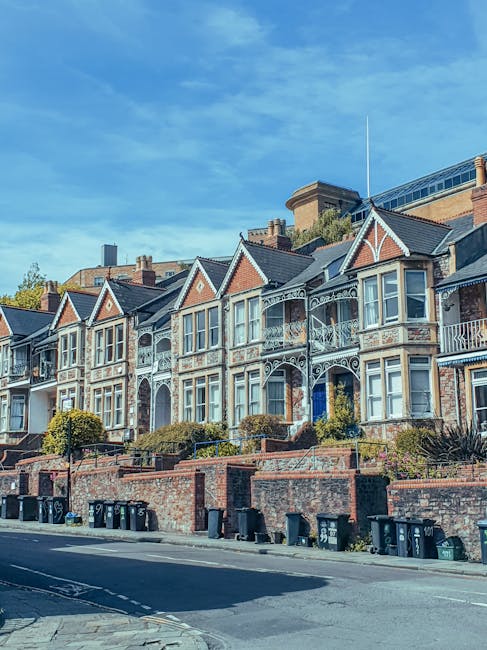 Photograph of a row of traditional Victorian terraced houses in Wimbledon Village, featuring ornate white cast-iron balconies, bay windows, and pitched roofs with brick and painted woodwork finishing.