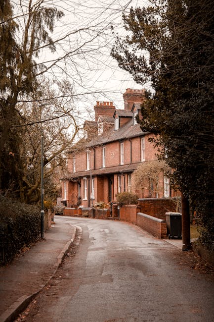Photograph of a row of traditional Victorian terraced houses in Wimbledon Village, featuring ornate white cast-iron balconies, bay windows, and pitched roofs with brick and painted woodwork finishing.